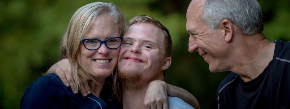 An older couple hugging a younger adult with trisomia