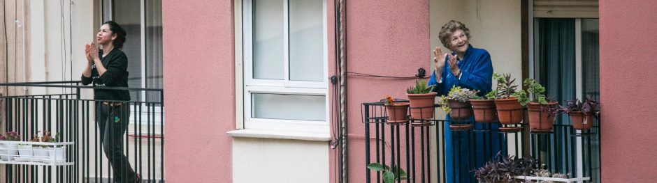 A young and an older women on two balconies, clapping hands. Photo Manuel Peris Tirado@Unsplash